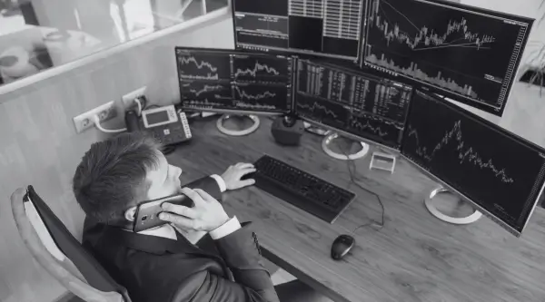 Business professional analyzing financial data on multiple computer screens for B2 First speaking test practice.